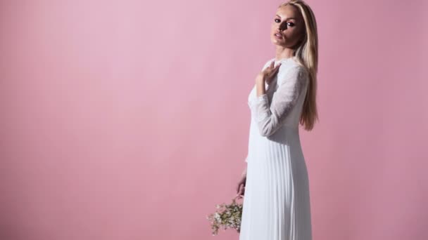 エレガントな白いドレスで金髪の若い女性 ハンドバッグを背景にポーズの女の子 春の花の花束を持つ女性 ファッション 花とのウクライナの女の子 — ストック動画