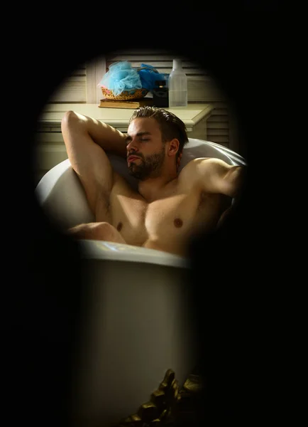 Man relax in bath seen in keyhole, secret