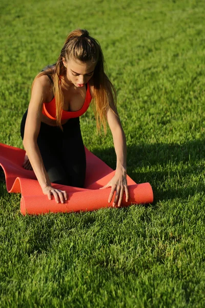 Jonge vrouw oprollen fitness mat op groen gras — Stockfoto