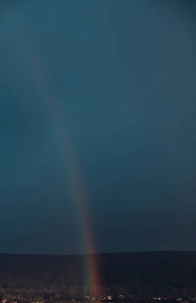 Rainbow above skyline with dark sky on background.