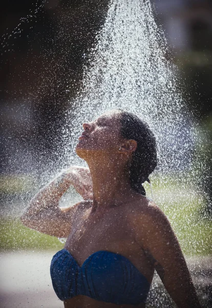Fiatal gyönyörű barna lány zuhanyozás, úszás után a strandon. Bikini szexi hölgy élvezi a zuhany a forró napsütésben. Hő- és frissítő koncepció. Víz csepp eső, vonzó nő. — Stock Fotó