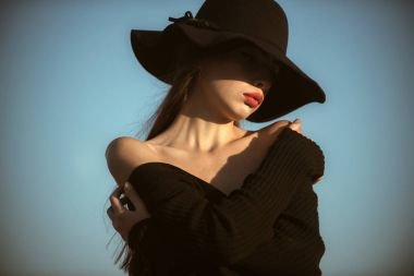 Zarif kadın kırmızı dudaklı. güneşli mavi gökyüzü arka plan üzerinde siyah şapkalı çıplak omuz ile zarif kadın