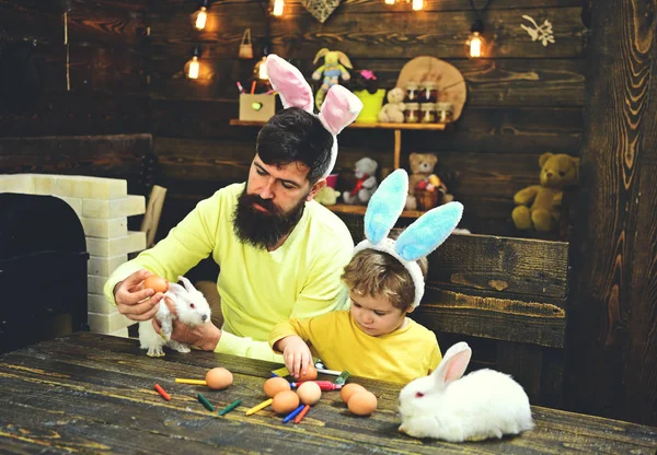 Easter family with fake bunny ears. Father and kid painting Easter eggs.