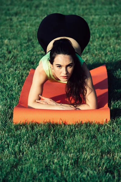 Fitness woman with ponytail doing plank position on green grass