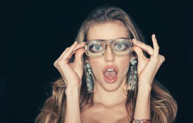 Optik mağaza konsepti. Kız kısa sightedness modern gözlük ihtiyacı var. Güzellik kız makyaj ve büyük küpeler takı, koyu arka plan ile. Sürpriz yüz kadınla vizyon için çirkin gözlük takmaz.