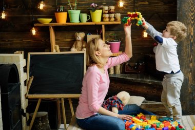 Kreş kara tahta arka plan ile. Anne ve oğlu Oluşturucu ile oynamak. Annelik kavramı. Evde Oluşturucu ile aile oynamak. Anne ve çocuk Oluşturucu, plastik tuğla ayrıntıları ile oynamak.