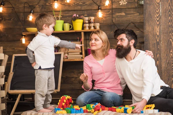 Dziecko z rodzicami grać z plastikowych klocków, budować budowlanych. Rodzice przytula, oglądanie syn gry, cieszyć się rodzicielstwa. Ojciec, matka i syn ładny grać z cegły Konstruktor. Koncepcja rodzicielstwa. — Zdjęcie stockowe