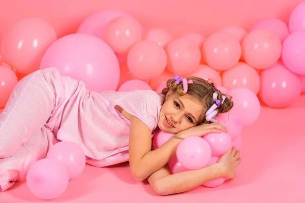 Klein meisje in een roze pyjama's speelt met ballonnen. — Stockfoto