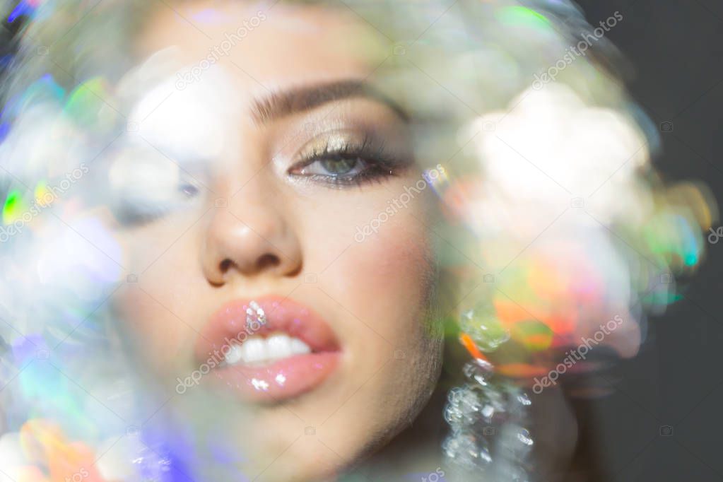 Woman with sensual lips looks sexy. Fashion and art concept. Beauty fashion girl with makeup, lipstick, eyeshadow, mascara, defocused, dark background. View through shimmering brilliant lens.