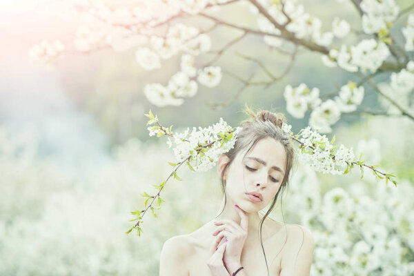 Girl or pretty woman with closed eyes on adorable face and white, blossoming flowers in hair in spring garden on sunny day on blurred floral environment. Youth and natural beauty