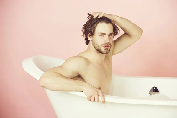 Joven guapo con cuerpo musculoso sentado en bañera blanca — Foto de Stock