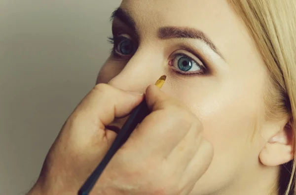 Mulher com olhos azuis recebendo maquiagem — Fotografia de Stock