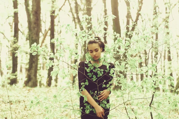 girl hiding in green tree leaves in spring forest