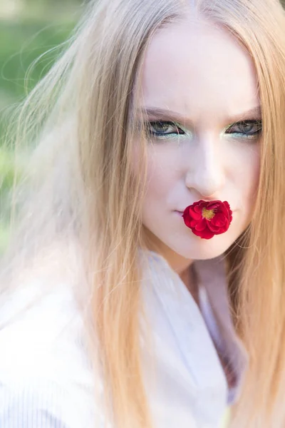 Dámské den, 8 březen, jaro koncept. Žena s červenou květinou v ústech, 8 březen. Modelka má dlouhé blond vlasy, účes na přírodu. Krásy dívka s glamour vzhled, make-up. — Stock fotografie