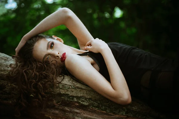 Frau mit langen brünetten Haaren entspannen auf Baum in der Natur. Frau mit lockiger Frisur im Sommer. Haarpflege, Therapie und Behandlung. Mädchen mit Make-up Gesicht, Schönheit. Mode-Model mit Glamour-Look — Stockfoto