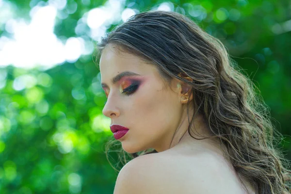 Donna con lunghi capelli castani sulla natura. Donna con acconciatura riccia e spalla nuda il giorno d'estate. Ragazza con il trucco viso, bellezza. Modella dal look glamour. Cura, terapia e trattamento dei capelli — Foto Stock