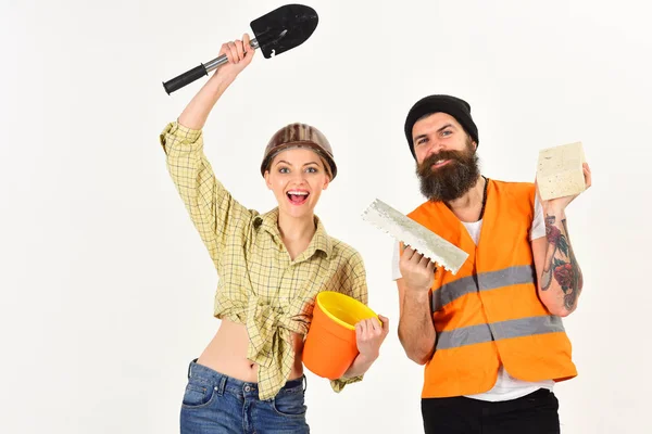 Reparateur met vriendin, kopie ruimte. Lachende vrouw in helm enthousiast over renovatie. Bouwers met bakstenen, schop en emmer, verliefde paar maakt het repareren van de witte achtergrond. Renovatie concept. — Stockfoto