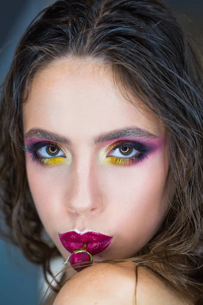 Schoonheid vrouw met glamour look, make-up en bloem in paarse lippen. Vrouw met rode roos in mond, womens dag. Mannequin met lange donkerbruine haren, kapsel. Womens dag, 8 maart, voorjaar concept — Stockfoto