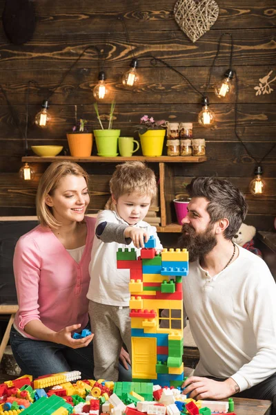 Kid with parents play with plastic blocks, build construction. Father, mother and cute son play with constructor bricks. Educational game concept. Family on busy face spend time together in playroom.