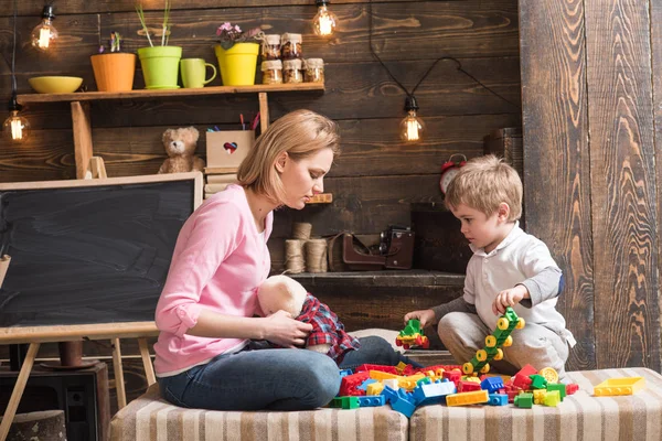 Motherhood concept. Family play with constructor at home. Mom and child play with details of constructor, plastic bricks. Nursery with chalkboard on background. Mother and son play with constructor.