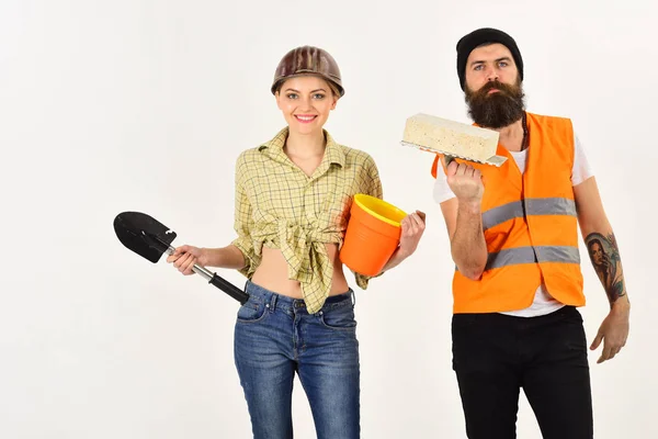 Bouwers met bakstenen, schop en emmer, verliefde paar maakt het repareren van de witte achtergrond. Reparateur met vriendin, kopie ruimte. Lachende vrouw in helm enthousiast over renovatie. Renovatie concept. — Stockfoto