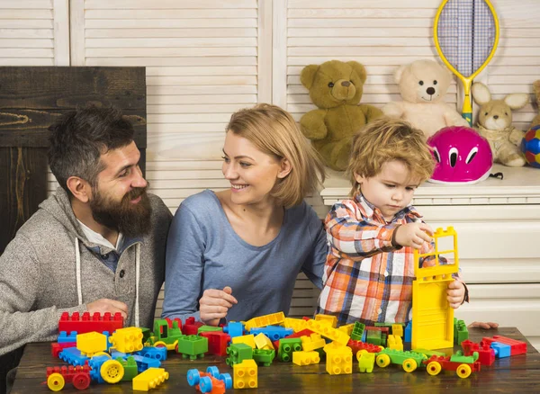Los padres con caras felices y el niño hace construcciones de ladrillo . —  Fotos de Stock
