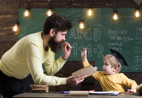 父亲, 老师看书, 教孩子, 儿子, 黑板上的背景。爸爸想长大的天才儿子。孩子的研究生帽喜欢听爸爸。神童和天才概念. — 图库照片