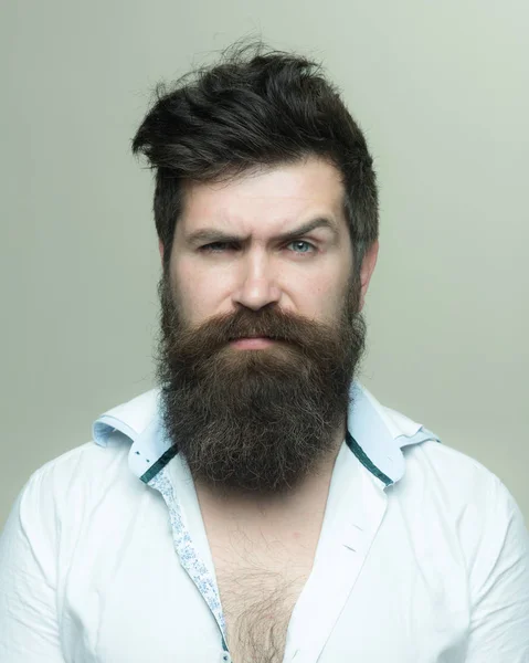 Conceito de barbearia ou cabeleireiro. Homem com barba longa, bigode e cabelo elegante, fundo claro. Macho no rosto estrito, usa camisa desabotoada. Cara com penteado moderno visitou cabeleireiro . — Fotografia de Stock