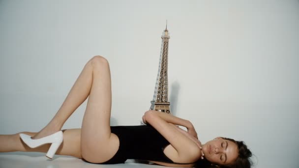 埃菲尔铁塔和美丽的女孩 在巴黎的工作室 优雅巴黎的年轻女人在黑色的衬衫和白色的鞋子 坐在地板上的埃菲尔铁塔附近 性格开朗的女孩梦想的旅游旅行浪漫法国 — 图库视频影像