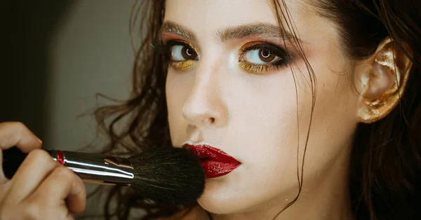 Woman use makeup brush, visage. Beauty model apply powder on face, cosmetics. Woman with art makeup and red lips, design. Girl skin, skincare, cosmetics. Visage course in beauty salon