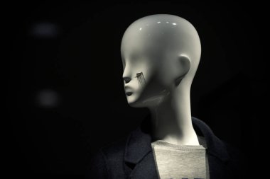 Kirpik koyu, siyah arka plan üzerinde manken. Giyim ve alışveriş kavramı. Beyaz plastik mankenler kat karanlık yaka ile baş. Şık lüks bebek parlayan.