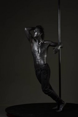 Pole dans adam dalgın yüzündeki metalik Kutbu, koyu arka plan ayakta. Kutubun adam çıplak gövde kutup dans performans ile taşır.