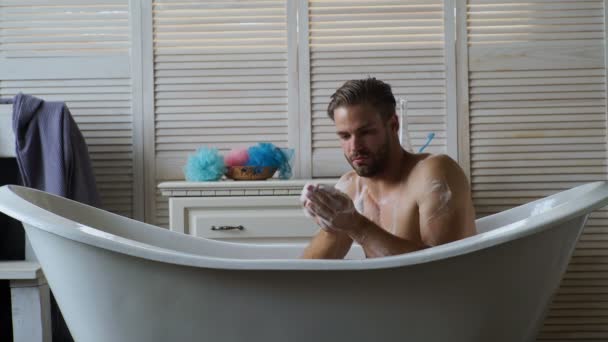 若いハンサムな男は浴槽でリラックスします 白い浴槽で風呂に入ってひげを持つ男 男性は 幸福とリラックスで高級バスタブで泡泡風呂で覆われています — ストック動画
