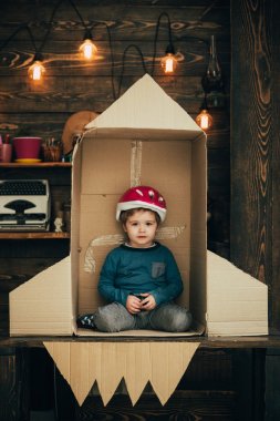 Çocuk kask içinde oturup karton el roket yapımı. Çocuk çocuk oyun kozmonot, astronot. Çocukluk kavramı. Roket, roket karton kutudan yapılan küçük kozmonot oturmak ile evde çocuk oyun.