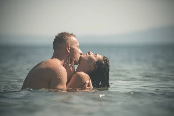 欲望の完全なカップルは、海を抱擁します。カップルの愛の抱擁と海の水の中でキスします。ハンサムな情熱的な恋人とブルネット。マッチョで裸の女の子大好きです。愛とロマンチックな概念. — ストック写真