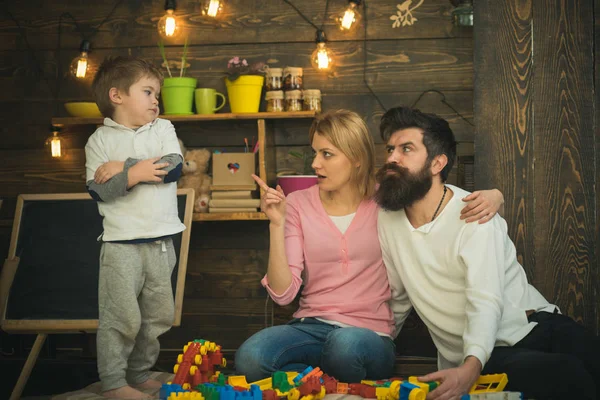 Kid with parents play with plastic blocks, build construction. Father, mother and cute son play with constructor. Parents hugs, strictly watching son playing, enjoy parenthood. Naughty boy concept. — Stock Photo, Image