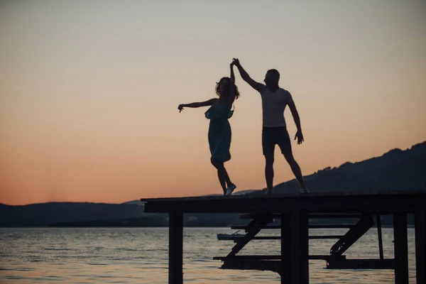 Romance and love concept. Silhouette of sensual couple dancing on pier with sunset above sea surface on background. Couple in love on romantic date in evening at dock, copy space. — Stock Photo, Image