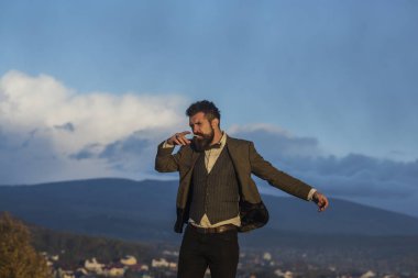 Hipster dramatik gökyüzü, önünde şık görünümü ile manzarası. Katı yüz papyon ile takım elbiseli adamla ücretsiz ve sigara geliyor. Manzara arka plan üzerinde ile sakallı adam. Özgürlük kavramı.