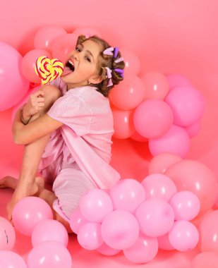 Çocukluk, mutluluk, tatlı rüyalar. Küçük kız çocuk üzerinde pembe lolipop yemek. Küçük kız candy lolipop ile. Diyet, doğum günü, punchy pastel, güzellik. Parti balonları, çocukta curlers, pijama moda.