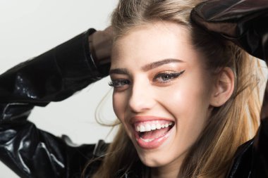 Bayan yağmurluk ya da yağmurluk poz, seksi kapatın. Uzun saçlı kız siyah pelerin, gri arka plan giyer. Kadın mutlu yüz çekici tapınaklar dokunursa, şık pelerin takıyor. Moda kavramı.