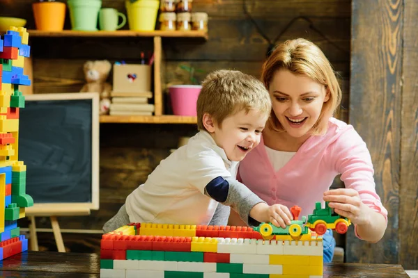 母性观念 金发碧眼的妈妈和儿子玩塑料积木火车 兴奋的学前儿童与他的微笑的母亲或幼稚园老师玩 — 图库照片