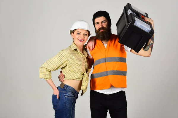 Bouwers met toolbox, verliefde paar maakt het repareren van de grijze achtergrond. Renovatie concept. Reparateur met vriendin, kopie ruimte. Lachende vrouw in helm enthousiast over renovatie. — Stockfoto