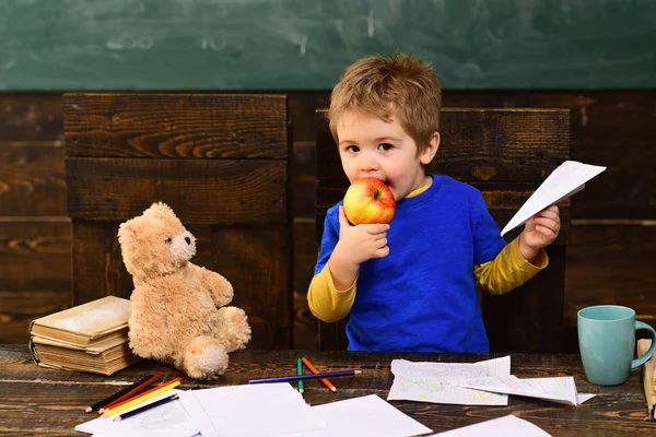 孩子吃多汁的苹果 手里拿着纸飞机的金发男孩 可爱的孩子在幼稚园 — 图库照片