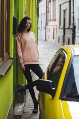 Sevimli genç yüzü olan kadın taksi şehirde alır. Şık elbiseleri Avrupa şehir duvarının yakınında duran kız. İnce gövde ve sakin yüz, tam uzunlukta bayanla. Şehir, Araba, taksi, moda, gençlik kavramı.