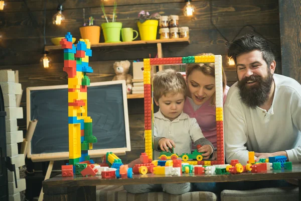 家庭在家里玩构造函数。父亲、母亲和儿子在大框架建筑附近玩耍, 用玩具砖、塑料块制作。母亲和可爱的儿子玩构造器。家庭时间概念. — 图库照片