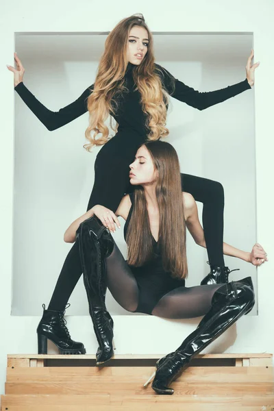 Fashionable ladies with make up and skinny legs posing, white background. Girls with long hair on mysterious faces posing in black clothes. Fashion and beauty concept. Ladies slim wear tight clothes.