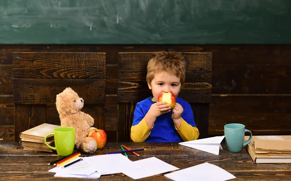 Шкільна перерва. Голодний хлопчик їсть яблуко в класі. Маленький хлопчик грає з паперовим літаком — стокове фото