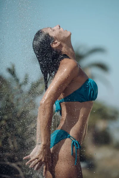 Pojęcie ciepła i orzeźwienia. Krople wody spadające na atrakcyjną kobietę. Młoda piękna dziewczyna brunetka pod prysznicem na plaży po kąpieli. Seksowna Pani w bikini cieszy się prysznic gorący słoneczny dzień. — Zdjęcie stockowe