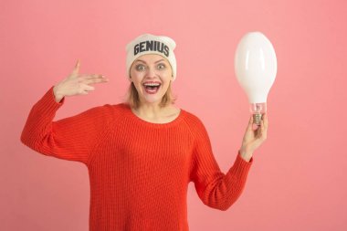 Woman with gun gesturer, has idea, pink background. Idea and creative concept. Lady with mad face holds lamp in hand, symbol of idea. Lady in hat with genius word, found out idea. clipart