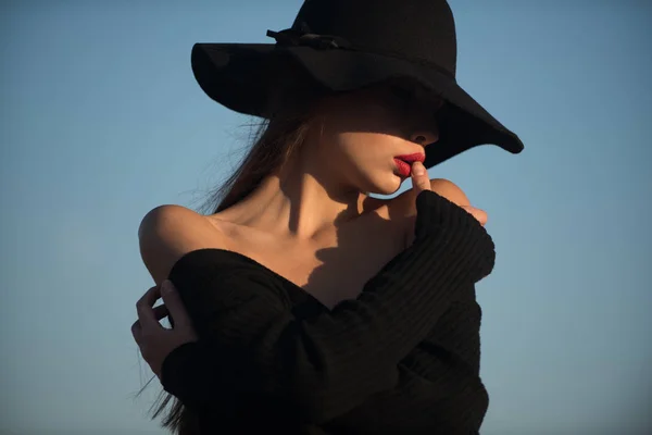 Retrato de mujer hermosa elegante en un vestido negro y sombrero ancho sobre fondo azul cielo —  Fotos de Stock